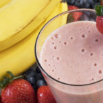 Smoothie next to fresh bananas, strawberries and blueberries