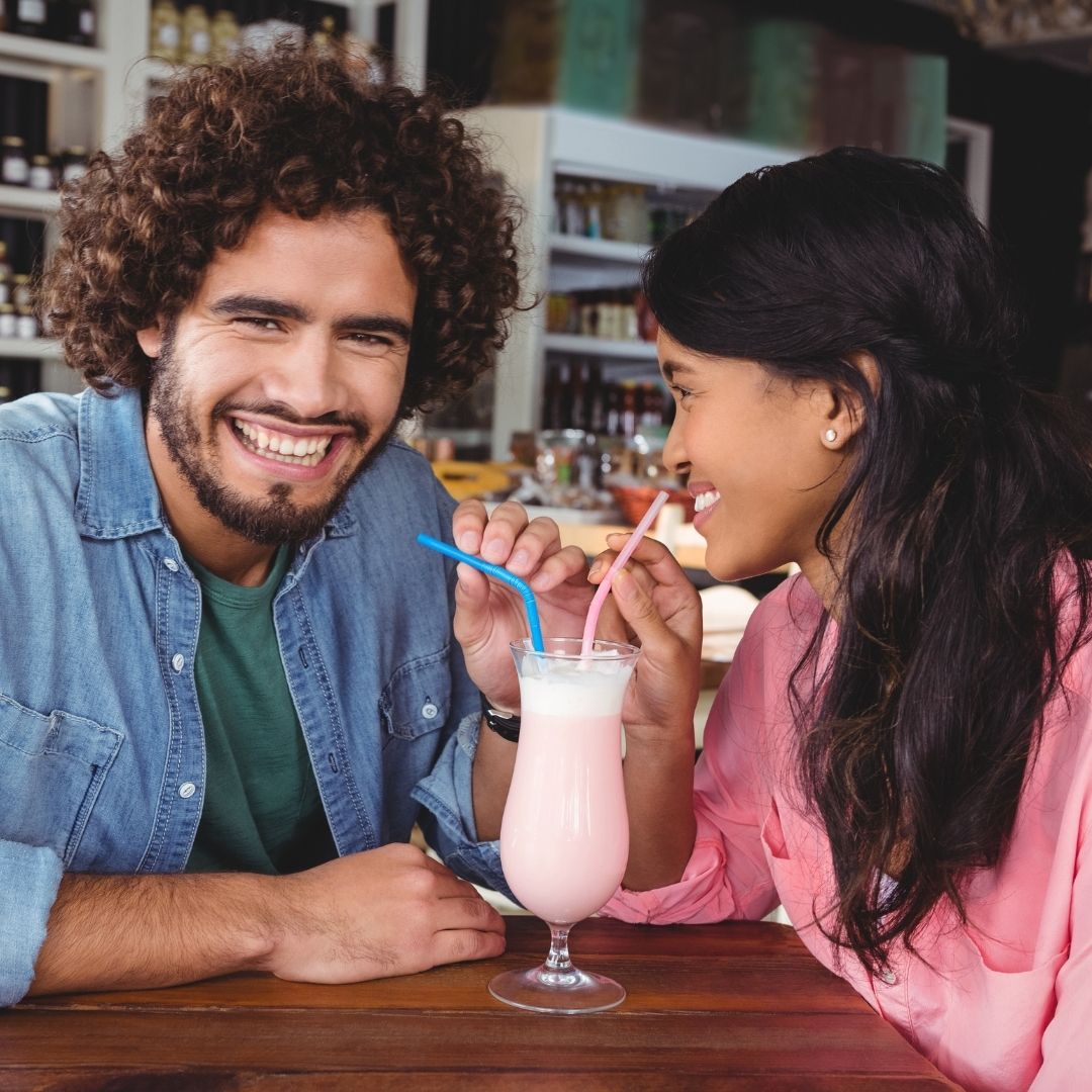 Couple smiling and sharing a strawberry milkshake at a diner